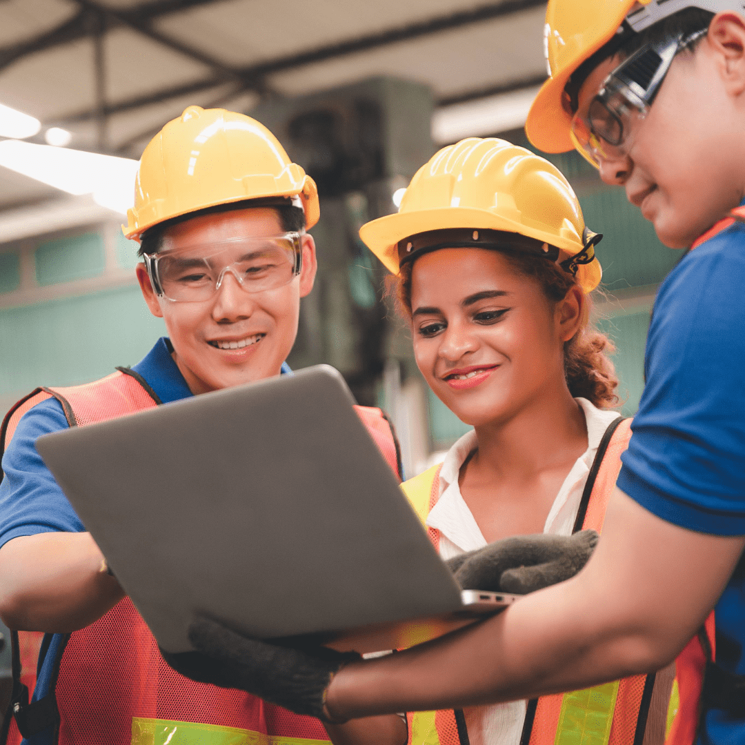 three people in hard hats looking at a laptop together